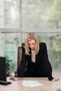 Young attractive Caucasian blond woman in black business suit sits at desk in bright office. Studying paper documents Royalty Free Stock Photo