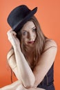 Young attractive caucasian brunette woman with bright blue eyes and dark lipstick, touches the black bowler hat, looking right to