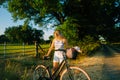 Young attractive caucasian woman with bicycle near horses pasture in summer day at sunset