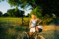 Young attractive caucasian woman with bicycle near horses pasture in summer day at sunset