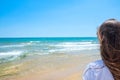 Young Attractive Caucasian Woman with Long Chestnut Hair with Back to Viewer Stands On Sand Beach Looks at Turquoise Sea Horizon Royalty Free Stock Photo