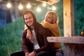 Young attractive cheerful couple sitting in front of wooden cottage. Woman leaning on to her boyfriend and hugging him. Beuatiful