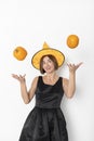 Young attractive and cheerful woman in black beautiful dress and witch hat throwing up two pumpkins isolated on white background Royalty Free Stock Photo