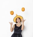 Young attractive and cheerful woman in black beautiful dress and witch hat throwing up two pumpkins isolated on white background Royalty Free Stock Photo