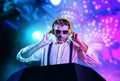 Young attractive and cool DJ in shirt and suspenders remixing music at night club using headphones in party strobo and flash Royalty Free Stock Photo