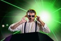 Young attractive and cool DJ in shirt and suspenders remixing music at night club using headphones in party strobo and laser Royalty Free Stock Photo