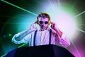 Young attractive and cool DJ in shirt and suspenders remixing music at night club using headphones in party strobo and laser Royalty Free Stock Photo