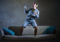 Young attractive and cool happy man listening to music with yellow headphones jumped on top of home sofa couch dancing internet so Royalty Free Stock Photo