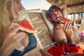 Young attractive couple enjoying vacation at beach, laying in sunbed eating watermelon. Holiday, fun, lesiure, lifestyle concept