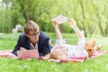 Young attractive couple wearing glasses is working or studying with laptop book note and pen lying on blanket in green park at sun Royalty Free Stock Photo