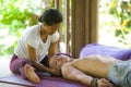 Young attractive and cute Asian woman giving traditional Thai massage to man lying on studio ground at tropical spa receiving Royalty Free Stock Photo