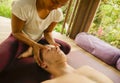 Young attractive and cute Asian woman giving traditional Thai massage to man lying on studio ground at tropical spa receiving Royalty Free Stock Photo