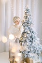 Young attractive dreamy blond woman, standing in front of decorated christmas tree and holding christmas present box Royalty Free Stock Photo