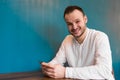 A young attractive European businessman in a white shirt and headphones spends time in a smartphone, sitting at a table in a cafe Royalty Free Stock Photo