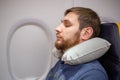Young attractive European man 30 years with a beard sleeping, resting using inflatable neck pillow in an airplane. Comfort, stress