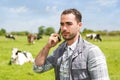 Young attractive farmer in a pasture with cows using mobile