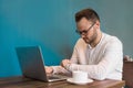 A young attractive fellow European businessman with glasses and a beard, looks time on smart clocks next to a laptop on a coffee