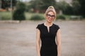 Young attractive female techer in black dress with sunglasses standing outside. Background of school Royalty Free Stock Photo