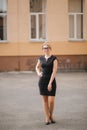 Young attractive female techer in black dress with sunglasses standing outside. Background of school Royalty Free Stock Photo