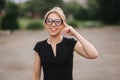 Young attractive female techer in black dress with sunglasses standing outside. Background of school Royalty Free Stock Photo