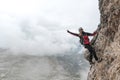 Young female climber on a vertical and exposed rock face smiling and making a peace sign