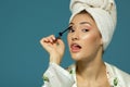 Young attractive funny woman putting eye mascara, studio shot over blue background, beauty treatment Royalty Free Stock Photo