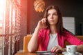 Young attractive girl, businesswoman, talking on mobile phone sitting alone in coffee shop . Happy female having rest in cafe. Royalty Free Stock Photo