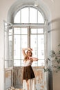 Young attractive girl in a dress in front of a large balcony window