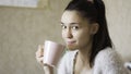 A young attractive girl drinks coffee from a pink cup while sitting on the bed at home Royalty Free Stock Photo