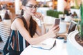 Young attractive girl in glasses does selfie using phone in cafe Royalty Free Stock Photo