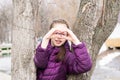 Young attractive girl in glasses makes a heart shape with her palms in front of her face in a city park in early spring Royalty Free Stock Photo