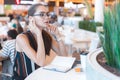 Young attractive girl in glasses uses bluetooth headset in cafe Royalty Free Stock Photo