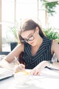 Young attractive girl in glasses writes in documents in cafe Royalty Free Stock Photo