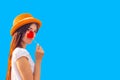 Young attractive girl with long hair and a straw hat holds a lollipop of a heart shape on a blue background, copy space Royalty Free Stock Photo