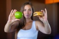 Young attractive girl is making choice between healthy and harmful food holding a green apple and a burger in her hands Royalty Free Stock Photo