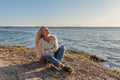 A young girl sits lounging on the shore of a pond and the wind blows her blond hair Royalty Free Stock Photo