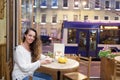 Young attractive girl sitting in the evening in a cafe with a Cup of tea to the backdrop of passing cars and city life. She looks Royalty Free Stock Photo