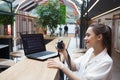 Young attractive girl is sitting in front of a laptop and holding a camera in her hands. Photographer and Retoucher