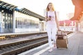 Attractive girl is standing with luggage at the station and waiting for the train, the student is going on a trip, she is walking Royalty Free Stock Photo