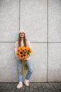 Young attractive girl stands against the background of white wall and holds bouquet of sunflowers in her hands Royalty Free Stock Photo