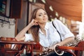 Young attractive girl in white shirt with a saxophone sitting on caffe shop - outdoor in street. young woman with sax looking Royalty Free Stock Photo