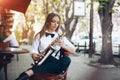 Young attractive girl in white shirt with a saxophone sitting near caffe shop - outdoor in sity. young woman with sax thinkin Royalty Free Stock Photo