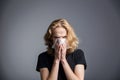 Young attractive guy with long hair and blue eyes blows his nose or sneezes into a handkerchief with a runny nose Royalty Free Stock Photo