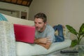 Young attractive handsome happy man lying at home couch working with laptop computer netbook relaxed in internet business concept Royalty Free Stock Photo