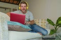 Young attractive and handsome happy man sitting at home sofa couch working with laptop computer and headphones using netbook rela Royalty Free Stock Photo