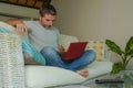 Young attractive and handsome happy man sitting at home sofa couch working with laptop computer netbook relaxed smiling cheerful i Royalty Free Stock Photo