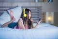 Young attractive and happy Asian Chinese woman with yellow headphones listening to music in mobile phone on bed at home smiling ha Royalty Free Stock Photo