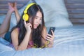 Young attractive and happy Asian Chinese woman with yellow headphones listening to music in mobile phone on bed at home smiling ha Royalty Free Stock Photo