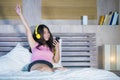 Young attractive and happy Asian Chinese woman with yellow headphones listening to music in mobile phone on bed at home smiling ha Royalty Free Stock Photo