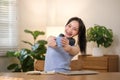 Young attractive happy Asian female student holding a cup of coffee sitting in the living room smiling and looking at Royalty Free Stock Photo